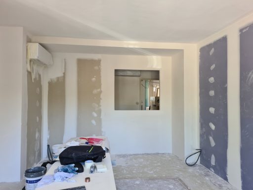 Intérieur en cours de rénovation, murs partiellement enduits et fenêtre visible.