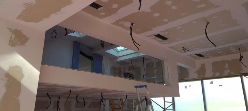 Intérieur en cours de rénovation avec murs en placoplâtre et câblage électrique visible.