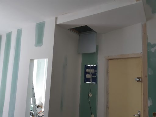 Mur inachevé avec des plaques de plâtre et une porte, reflet dans un miroir.